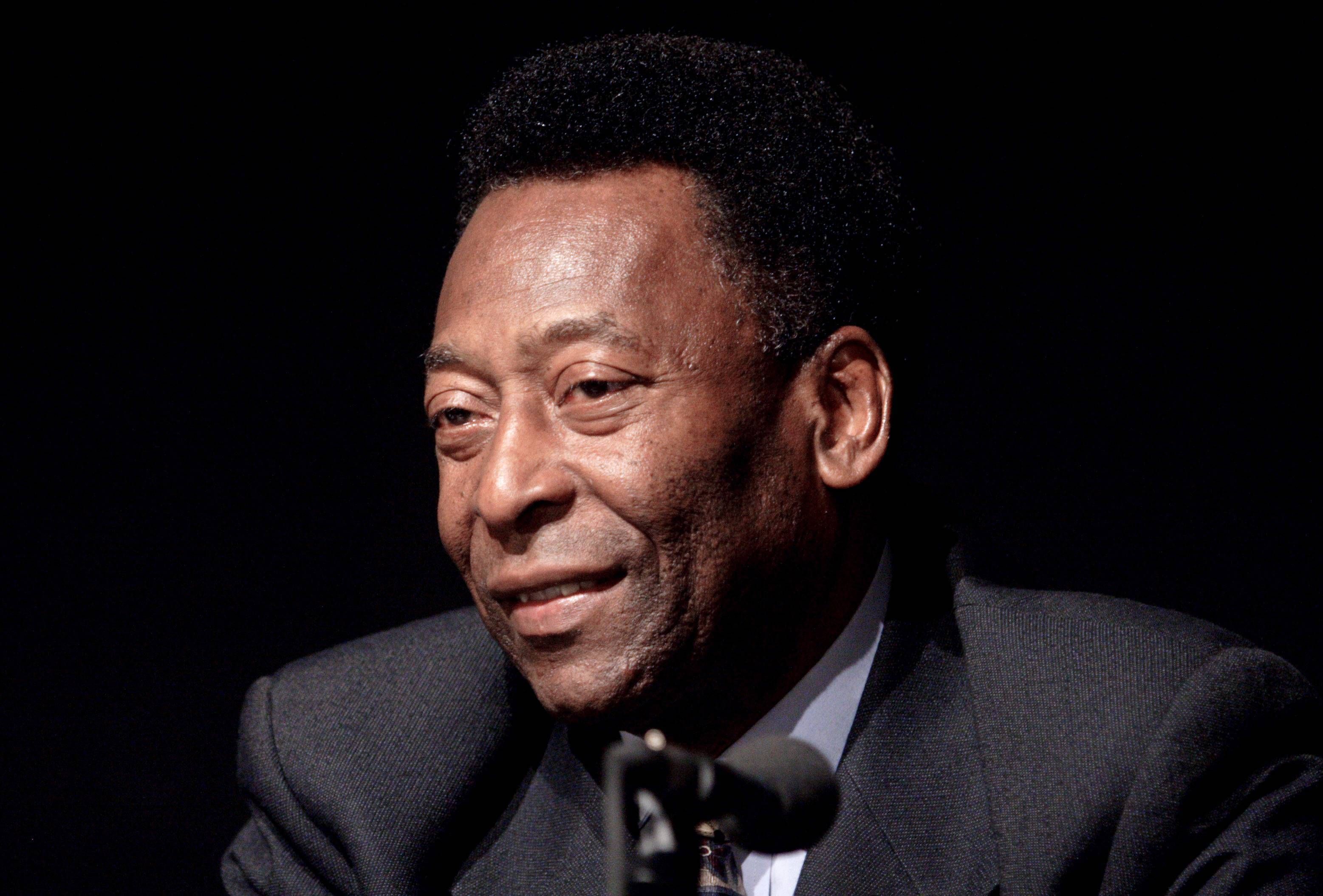 Pelé sitzt in schwarzem Anzug auf einem Podium, er lächelt leicht.