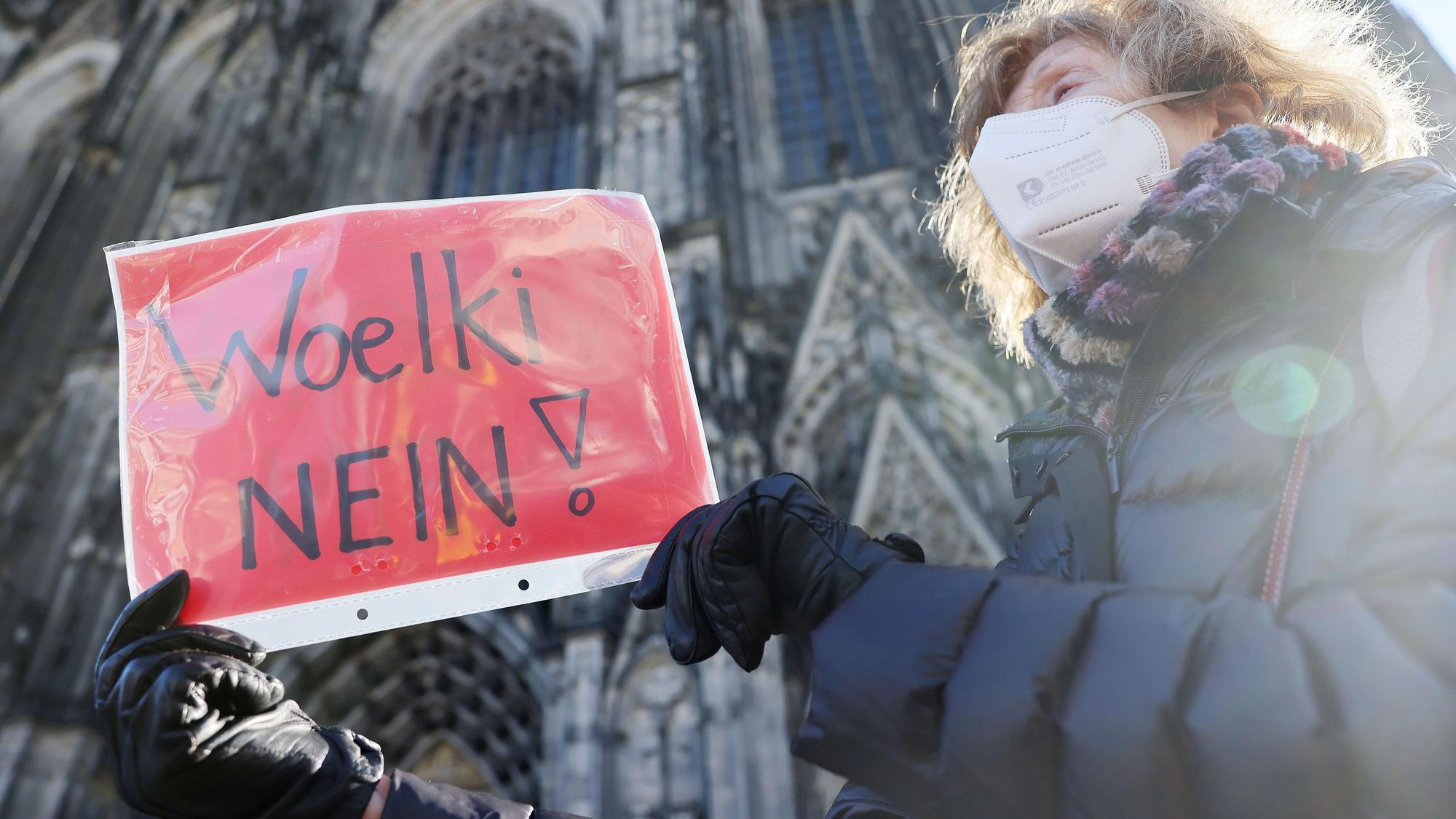 Eine Frau nimmt mit einem Plakat mit der Aufschrift „Woelki Nein!“ an einer Kundgebung der kirchenkritischen Bewegung Maria 2.0 gegen Kardinal Rainer Maria Woelki teil. Im Hintergrund ist der Kölner Dom zu sehen.
