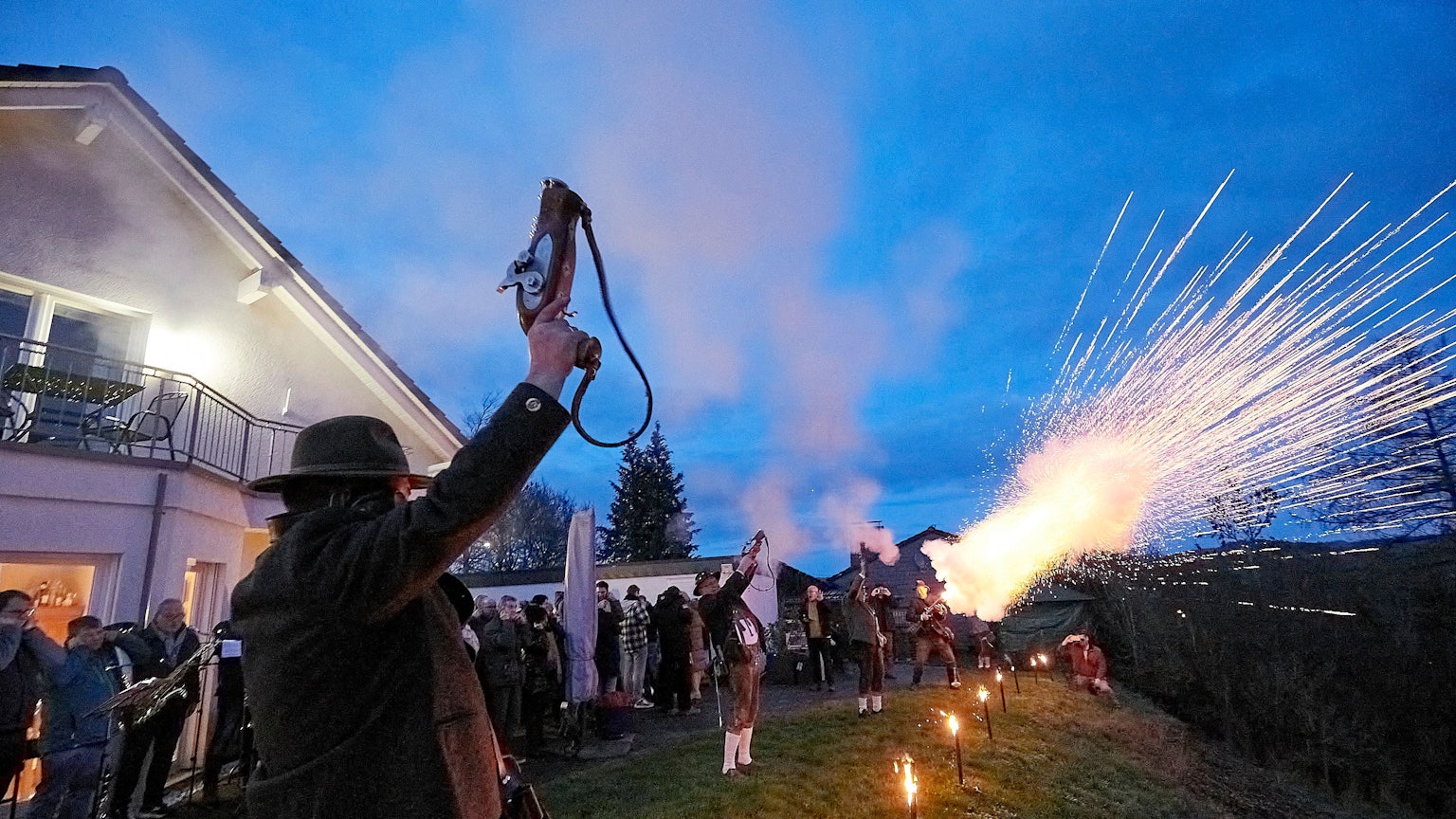 Das Foto zeigt den Moment, als sich die speziellen Böllerpistolen der in Trachten gekleideten Schützen mit Blitz, Rauch und mächtigem Getöse in den Abendhimmel entladen.