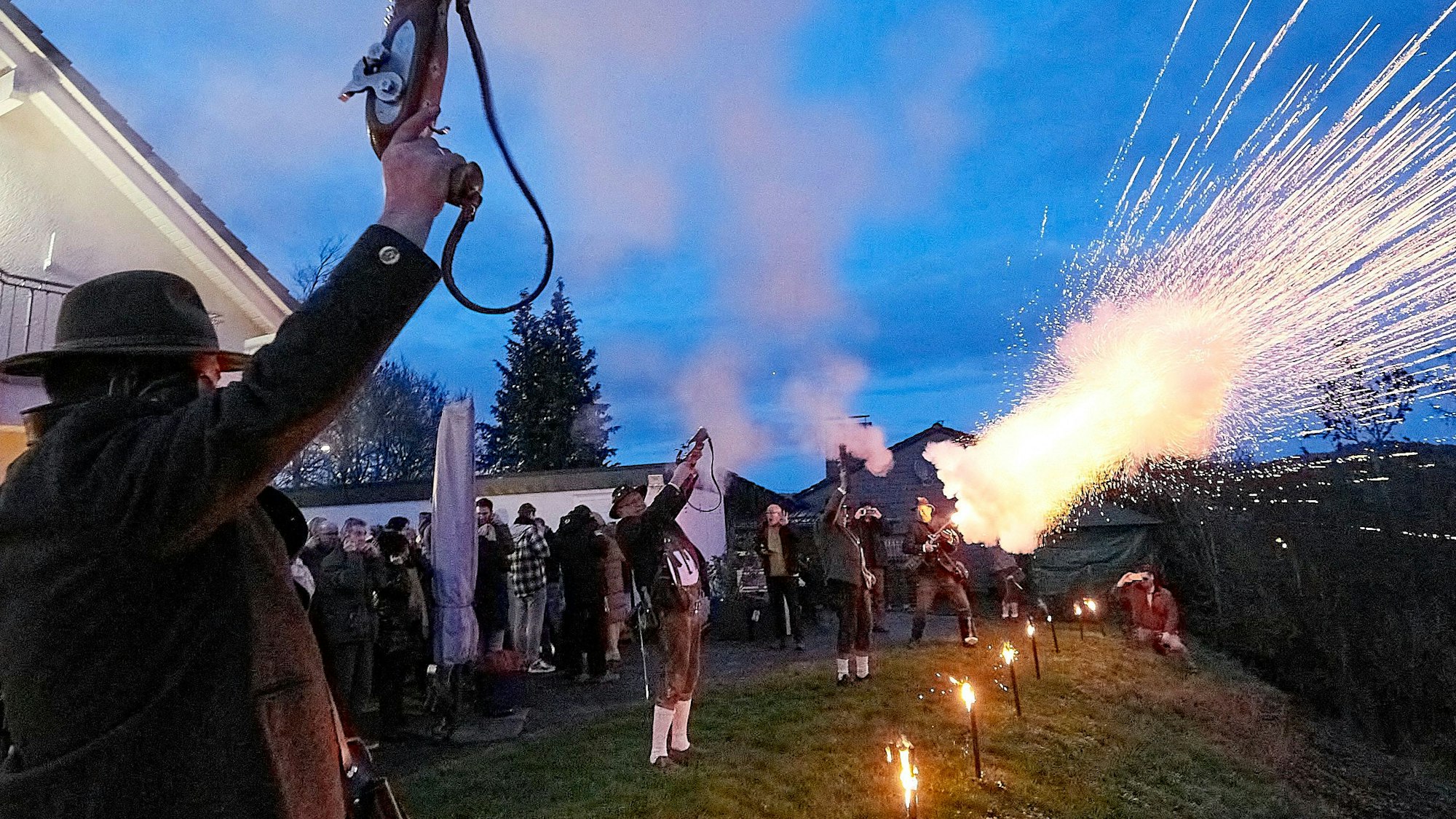Das Foto zeigt den Moment, als sich die speziellen Böllerpistolen der in Trachten gekleideten Schützen mit Blitz, Rauch und mächtigem Getöse in den Abendhimmel entladen.