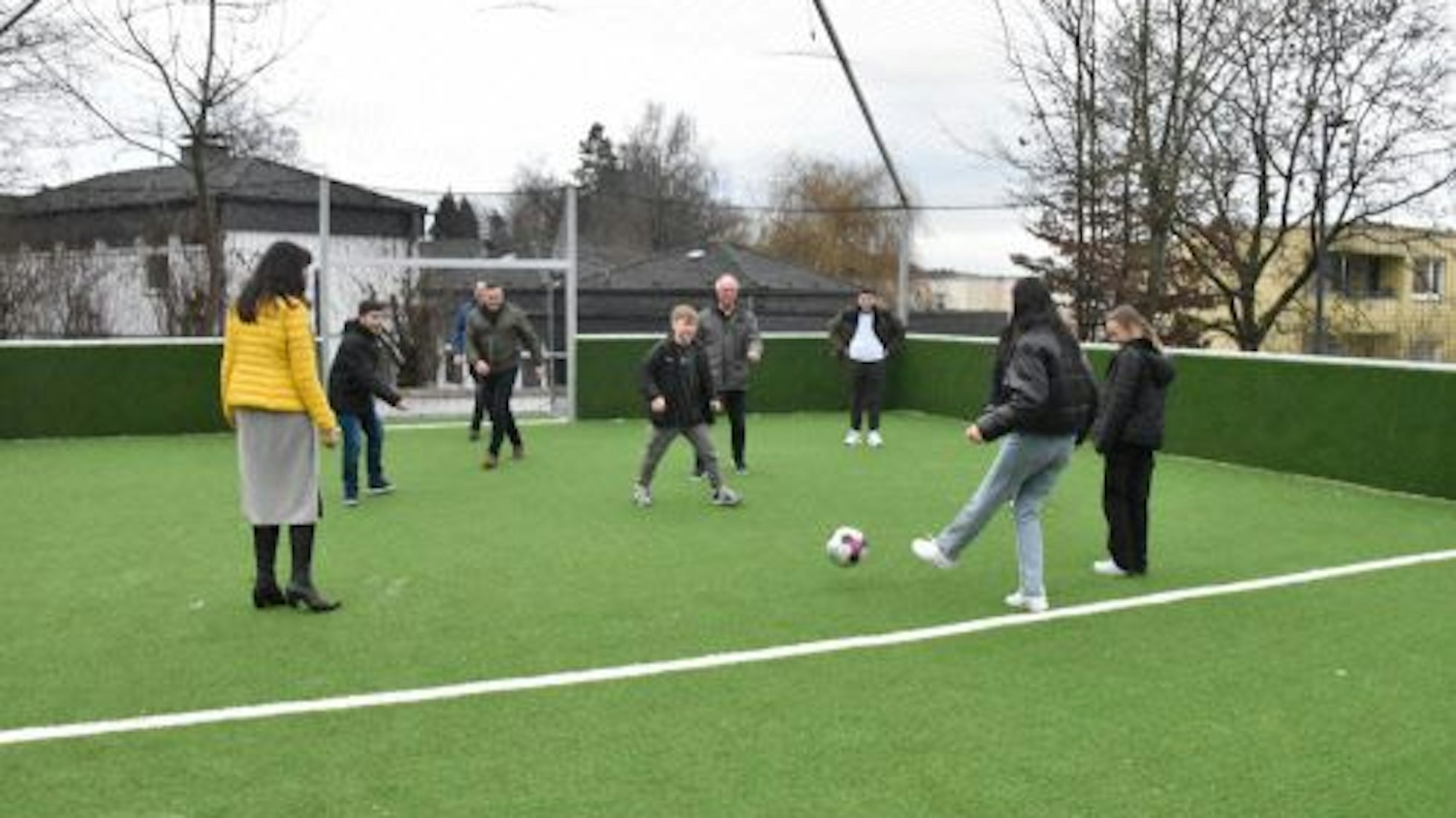 Auf einem Kunstrasenplatz spielen Jugendliche und Erwachsene Fußball.