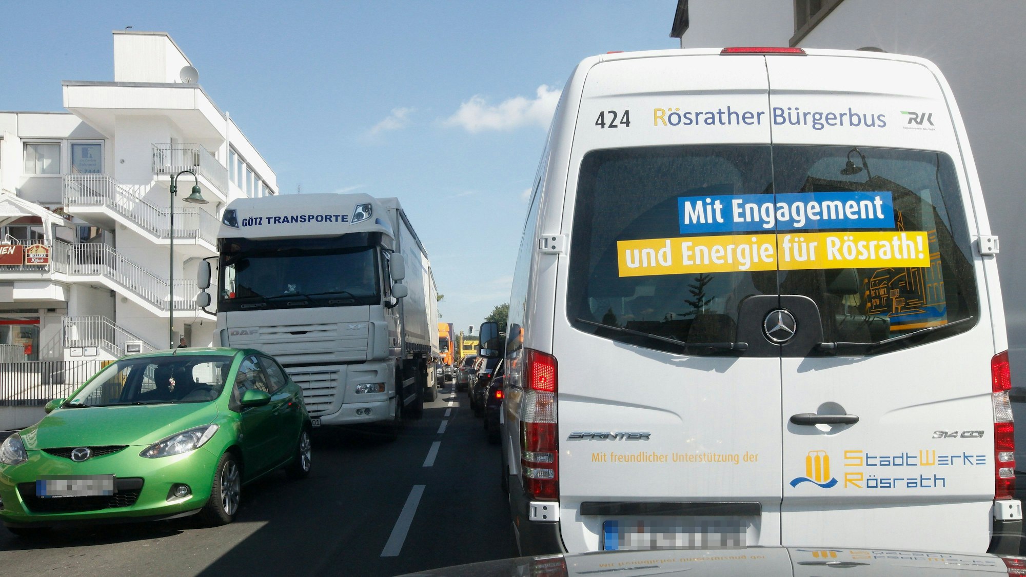 Der weiße Bürgerbus steckt im Verkehr zwischen Autos und Lkw.