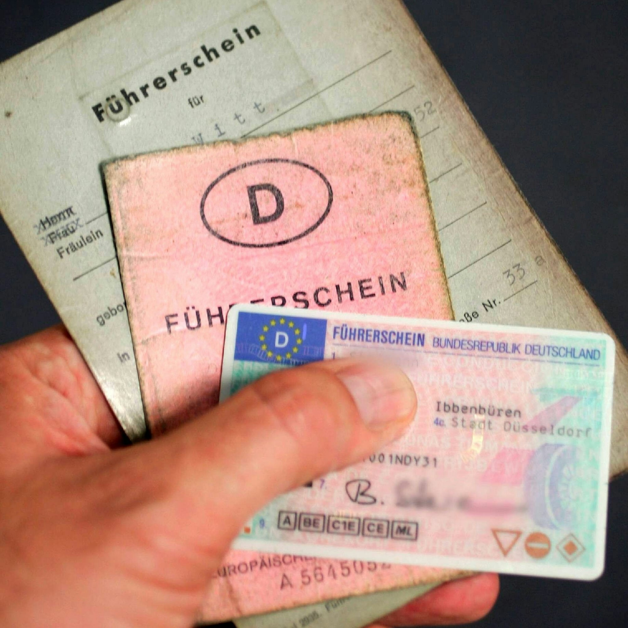 Eine Hand hält Führerscheine aus mehr als 60 Jahren: Vom grauen Lappen zur Scheckkarte.