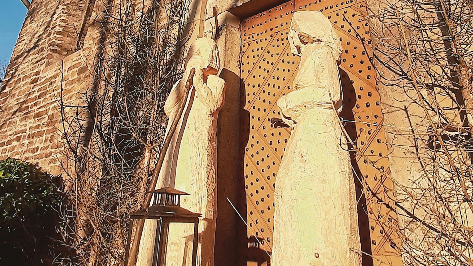 Zwei große Holzfiguren stehen vor einer steinernen Kirche.