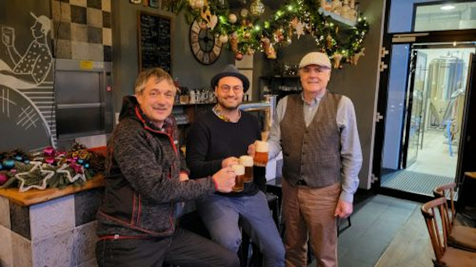 Drei Männer stoßen mit Bier in einer Gastwirtschaft an.