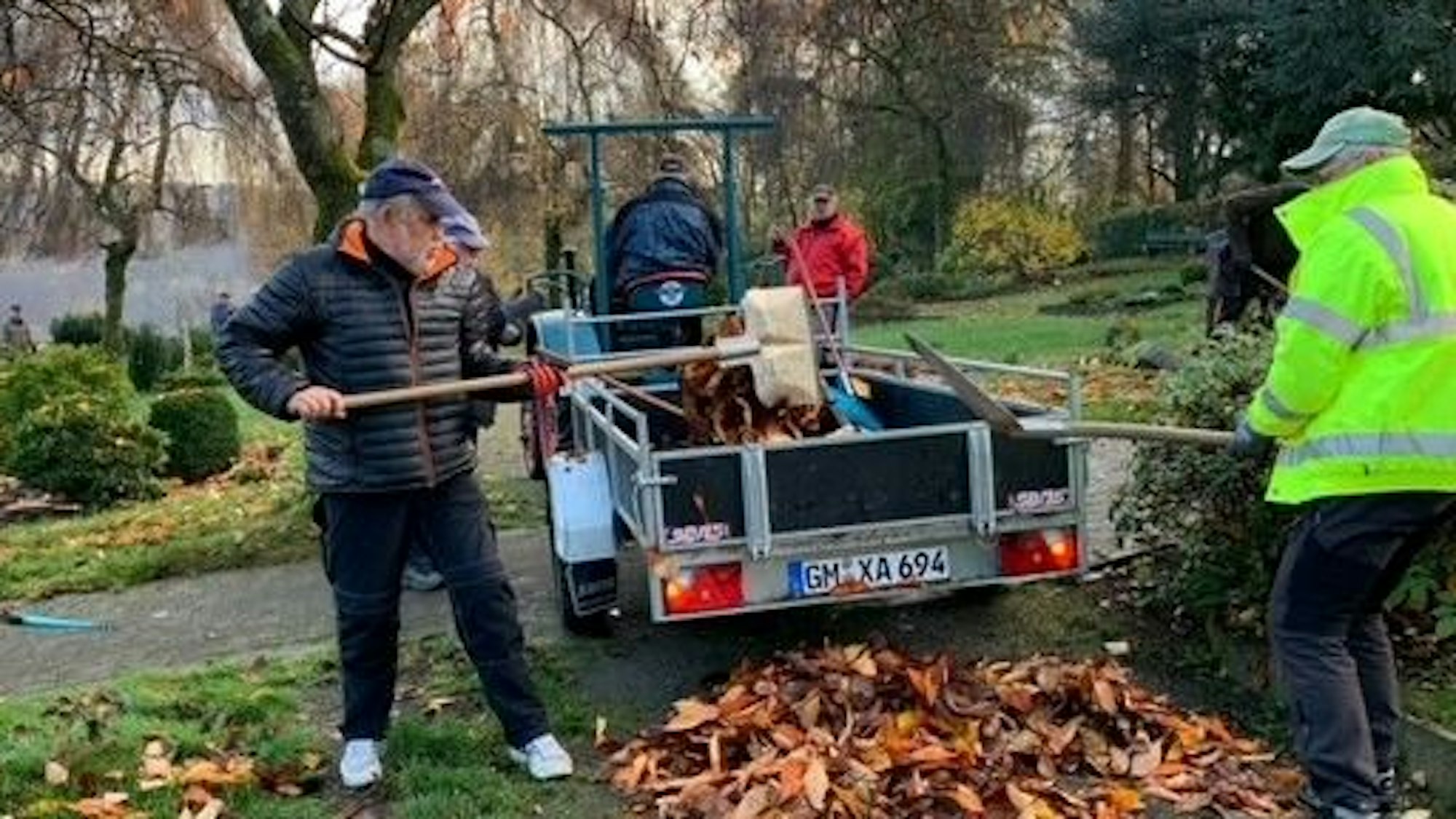 Blick auf zwei Männer, die mit Schaufeln Laub auf den Anhänger eines Traktor laden.