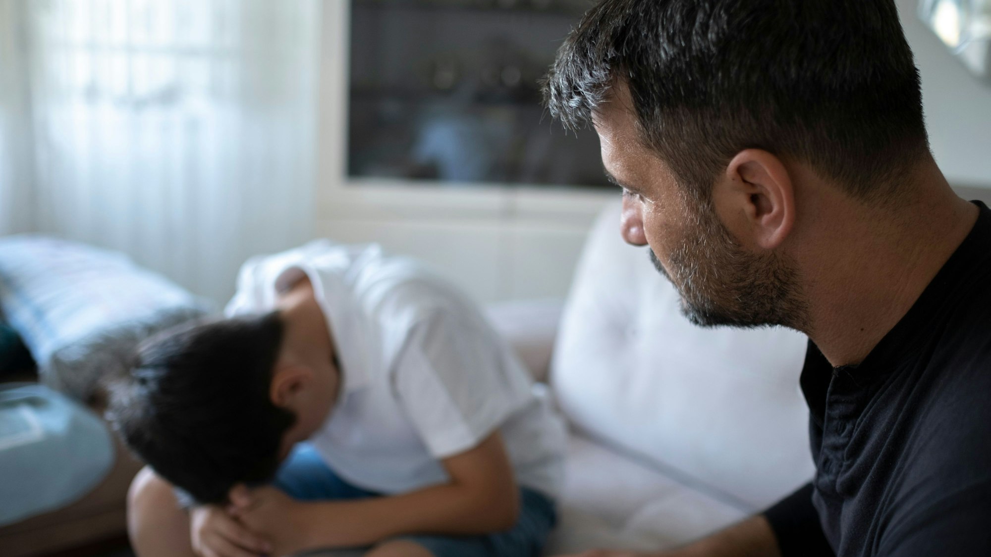 Mittelalter Mann schaut einen traurigen Jugendlichen an.