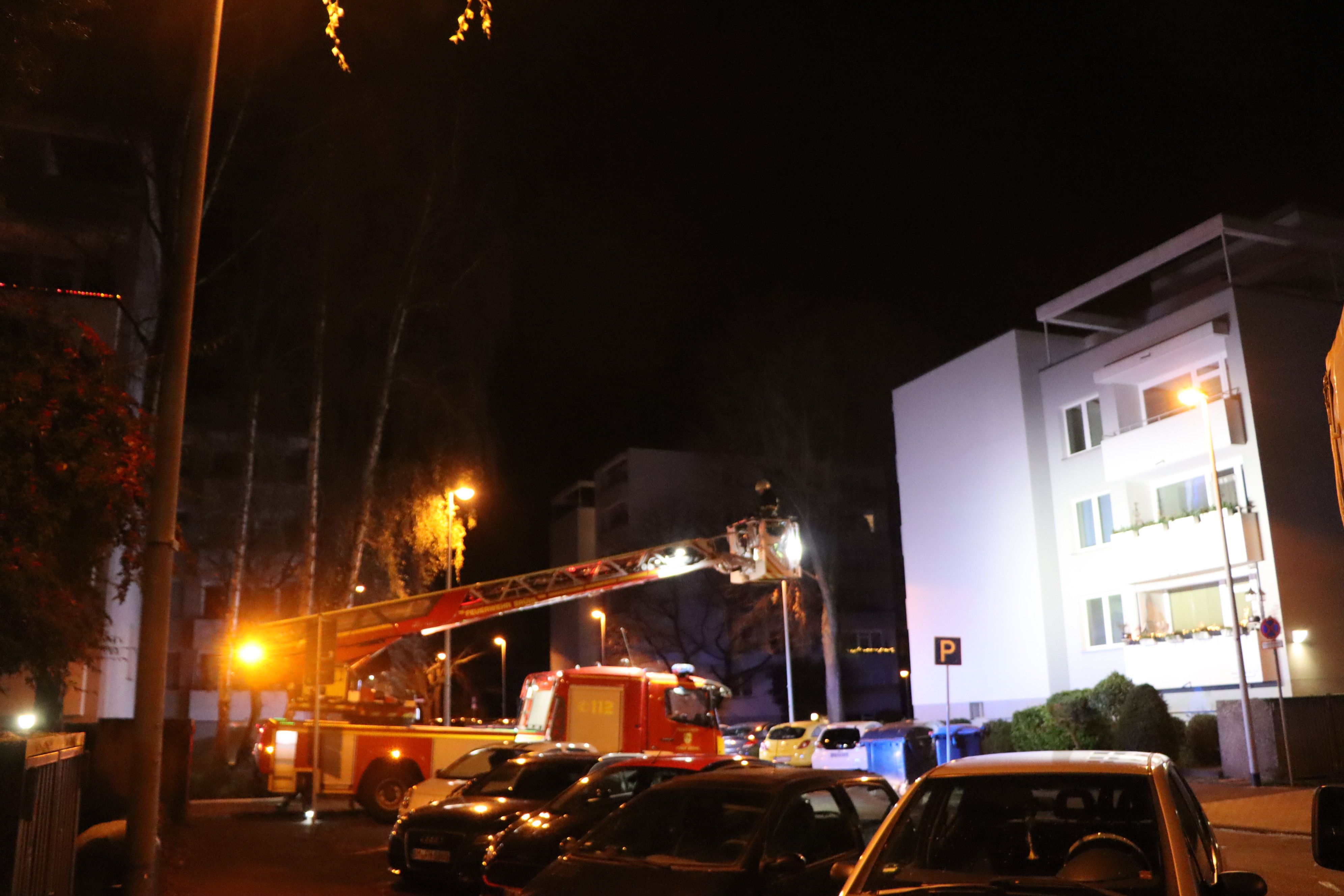 Die Feuerwehr dringt mit einer Drehleiter zum brennenden Mehrfamilienhaus in Brühl vor. Die weiße Fassade ist in der Dunkelheit angestrahlt.