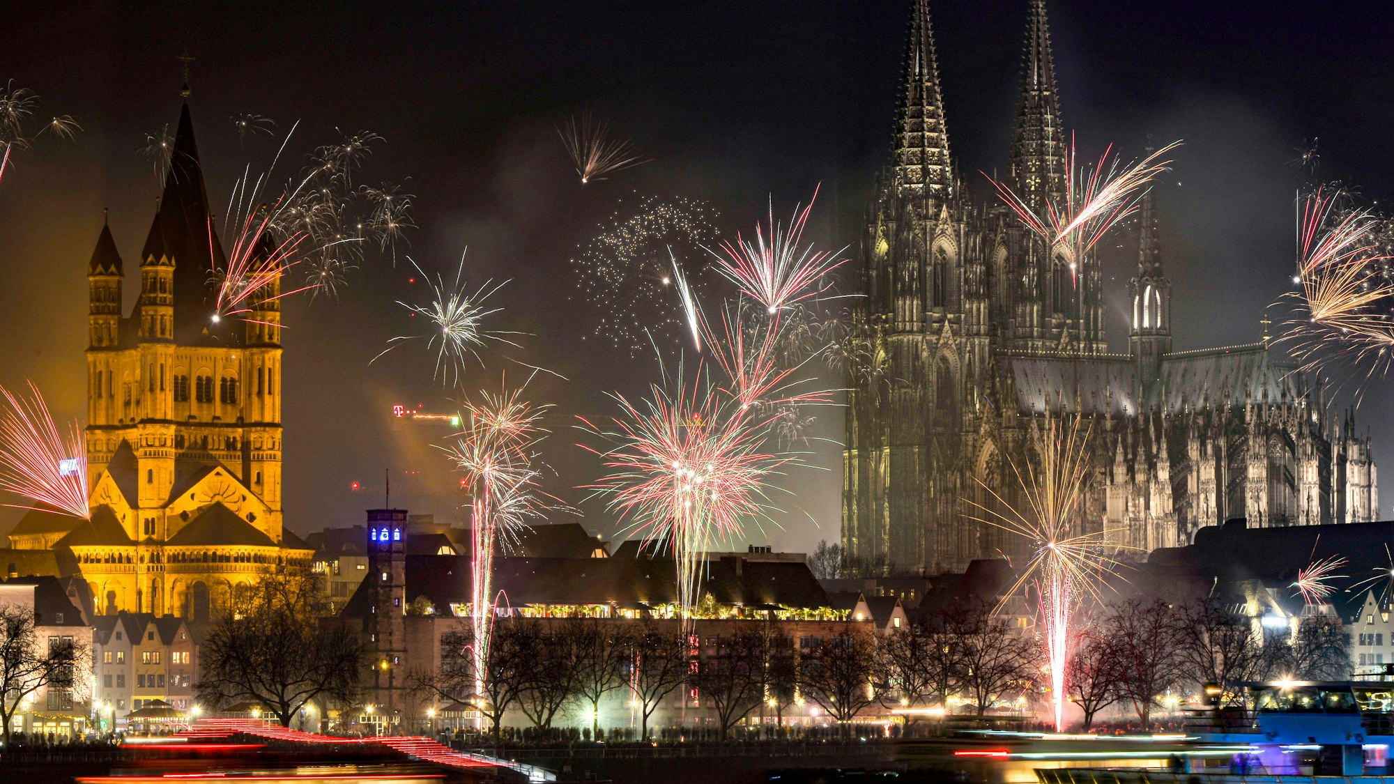 Lichtermeer am Nachthimmel von Köln. Das Silvesterfeuerwerk 2019 mit Blick auf den Dom. Im unteren Bildrand der prall gefüllte Rheinboulevard.