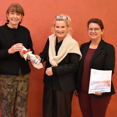 Die vier Frauen stehen vor einer roten Wand, sie halten das Workbook in ihren Händen.