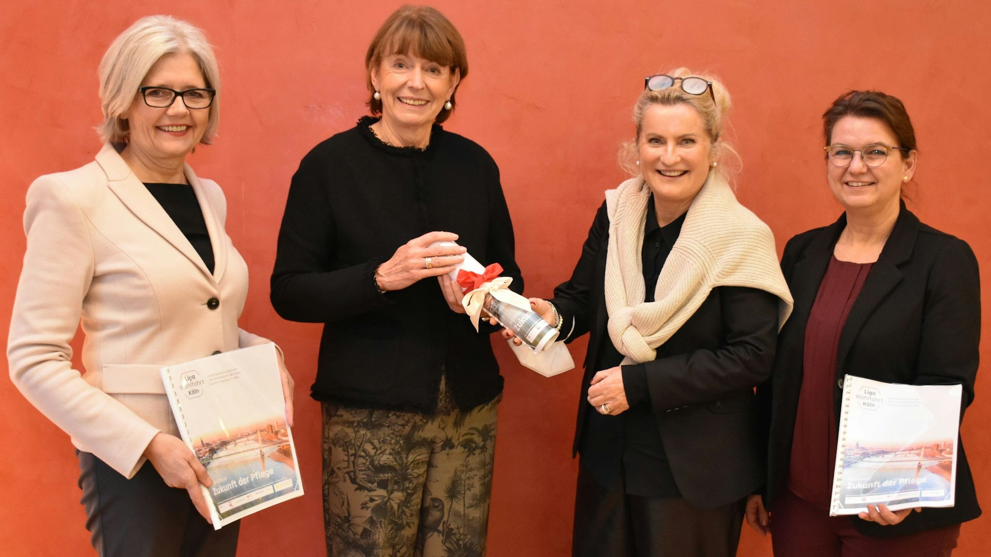 Die vier Frauen stehen vor einer roten Wand, sie halten das Workbook in ihren Händen.