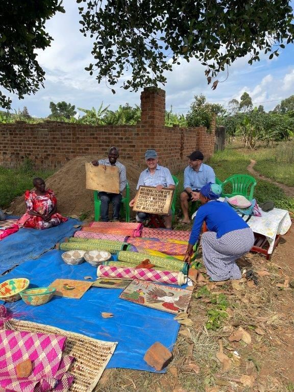 Franz Schwope inmitten von Menschen aus Uganda, vor ihnen bunte Decken und Matten