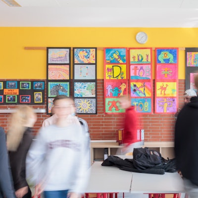Schülerinnen und Schüler in einem Klassenzimmer mit bunten Bildern an den Wänden. Die Kinder sind verschwommen fotografiert und unkenntlich.