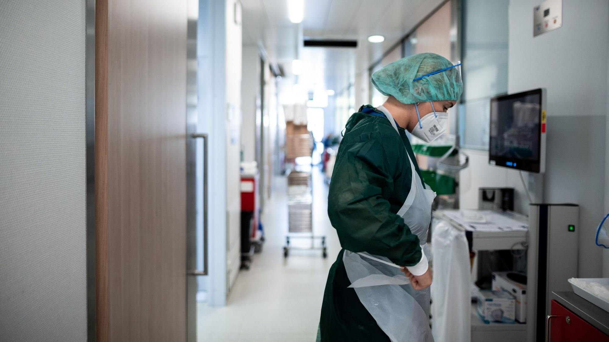 Eine Mitarbeiterin der Pflege steht auf dem Gang einer Corona-Intensivstation Schutzkleidung an.