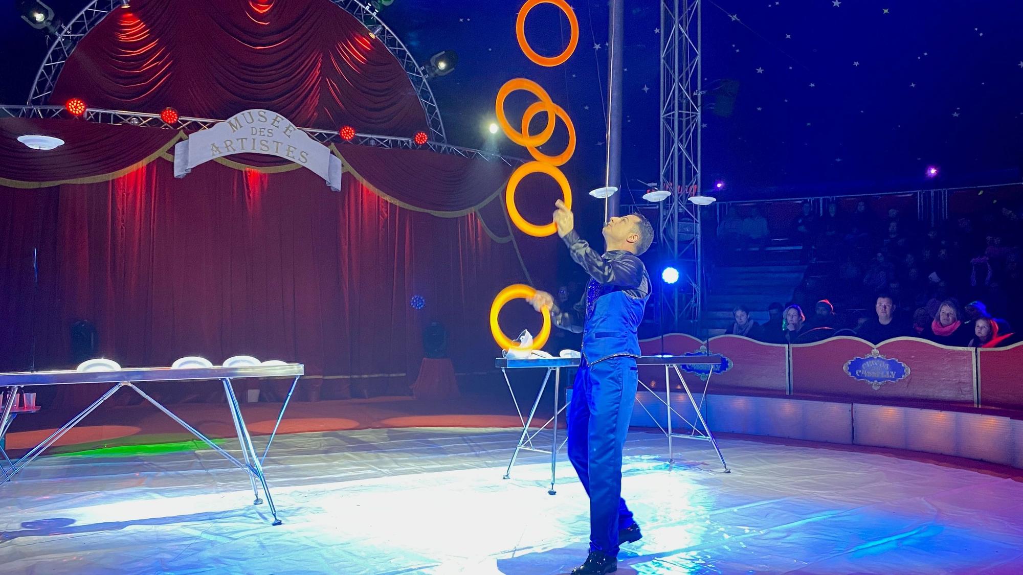 Mann jongliert in einer Manege mit fünf Ringen