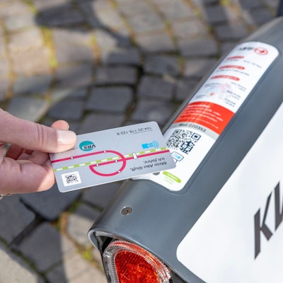 Eine Hand hält eine Abo-Karte der KVB zum Ausleiehen an die Verkleidung eines Leihrads.