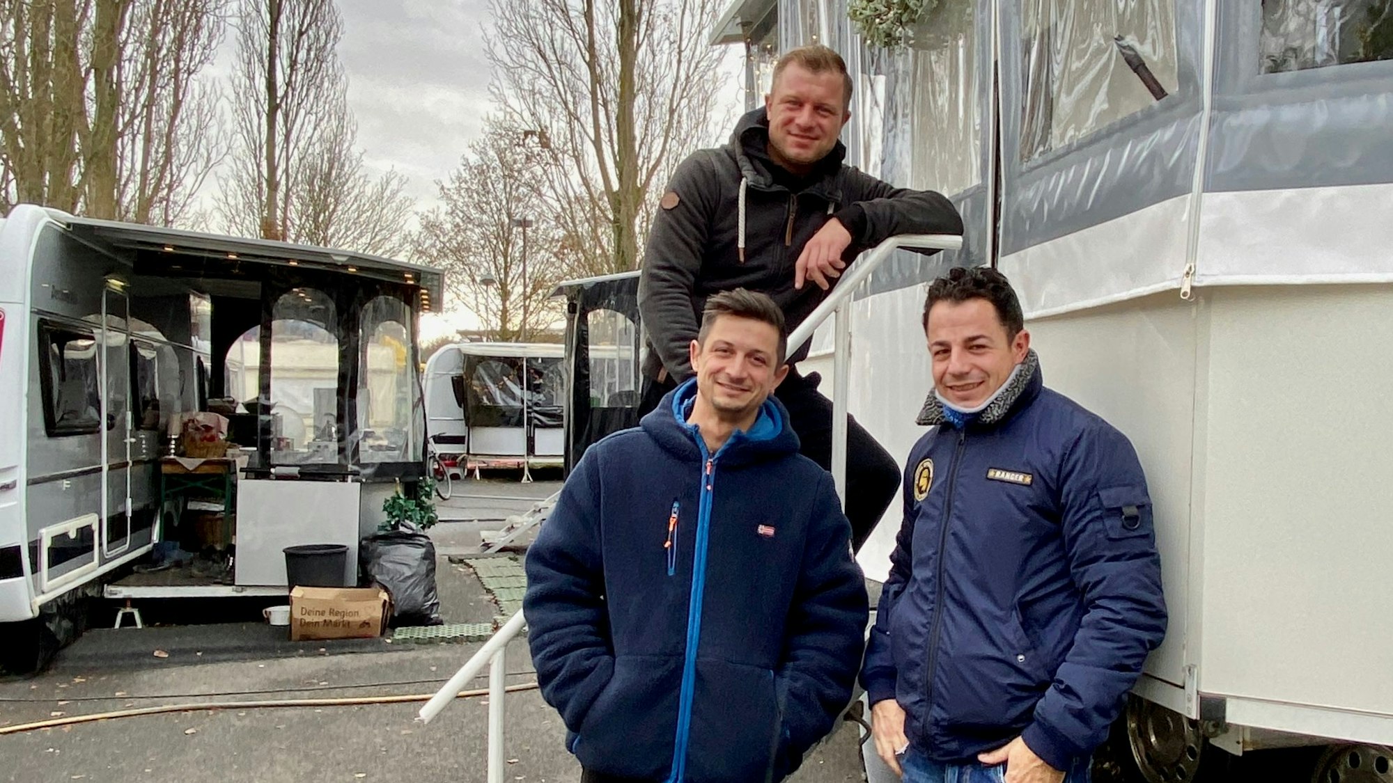 Drei Männer stehen vor einem Wohnwagen