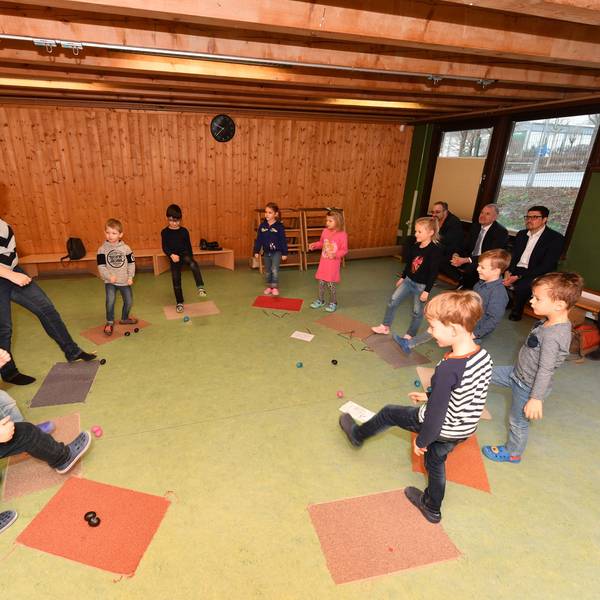 Kinder und eine Erzieherin stehen in einem Kreis und heben ihre Beine.