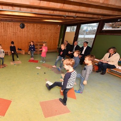 Kinder und eine Erzieherin stehen in einem Kreis und heben ihre Beine.