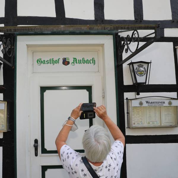 Eine Frau fotografiert mit ihrem Handy den Schriftzug „Gasthof Aubach“ an der Tür des Fachwerkhauses in Kürten-Olpe-