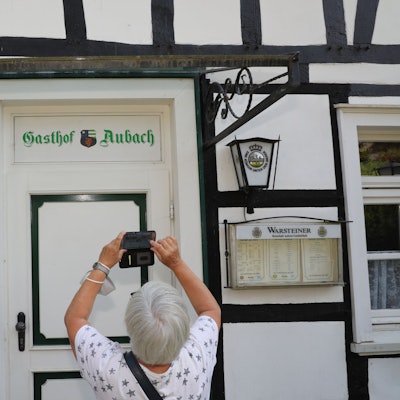 Eine Frau fotografiert mit ihrem Handy den Schriftzug „Gasthof Aubach“ an der Tür des Fachwerkhauses in Kürten-Olpe-