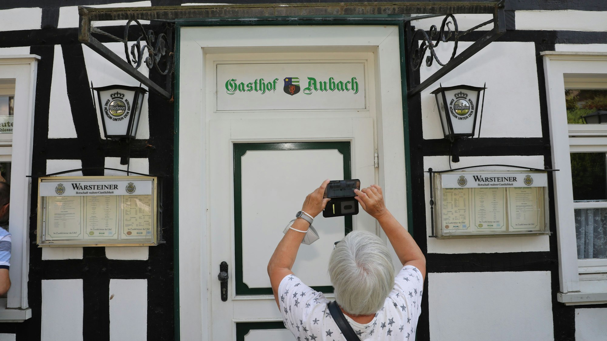 Eine Frau fotografiert mit ihrem Handy den Schriftzug „Gasthof Aubach“ an der Tür des Fachwerkhauses in Kürten-Olpe-
