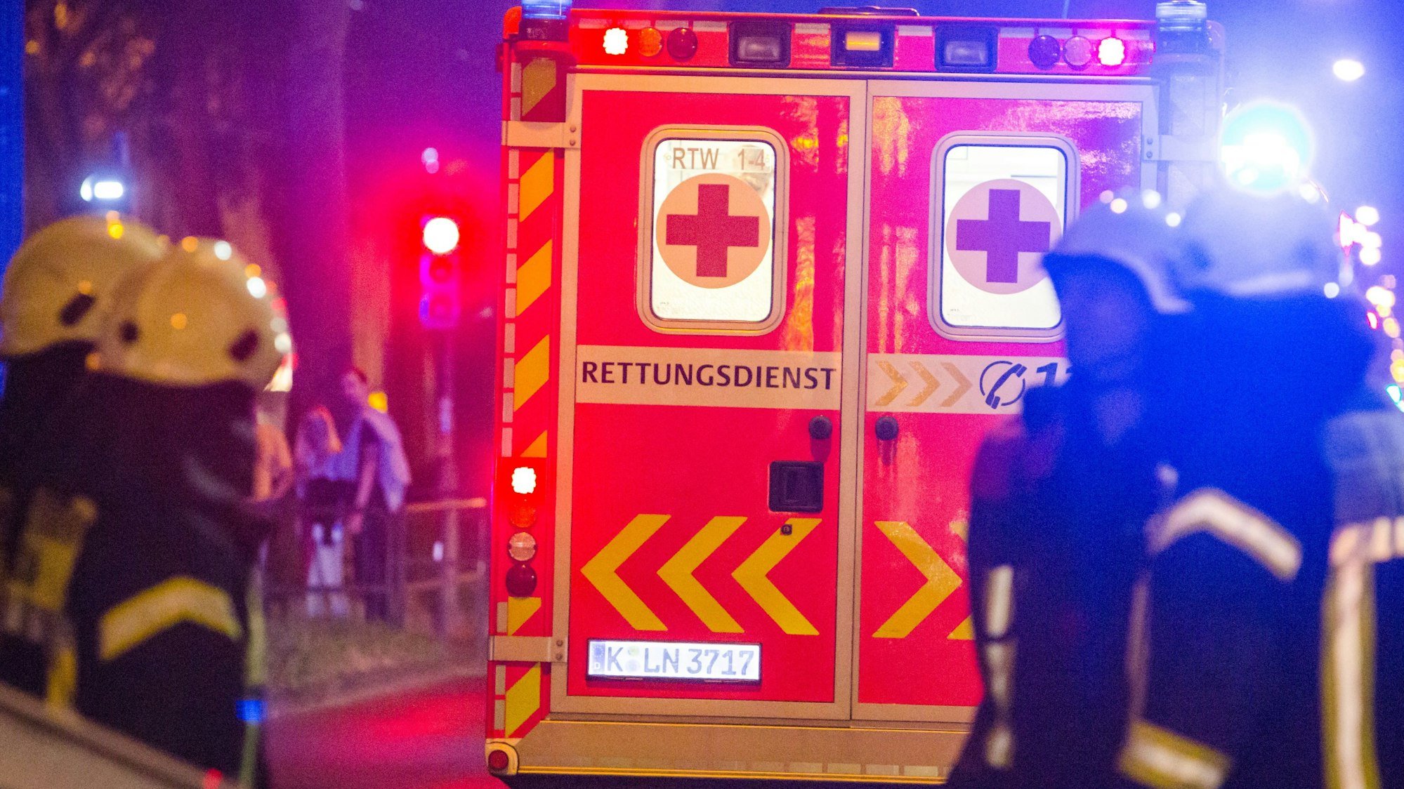 Feuerwehrleute stehen nachts hinter einem Rettungswagen.