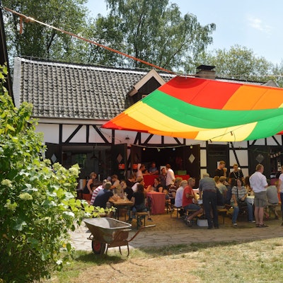 Menschen sitzen vor dem Kochshof und unter einem bunten Segel beim Patentreffen 2019.