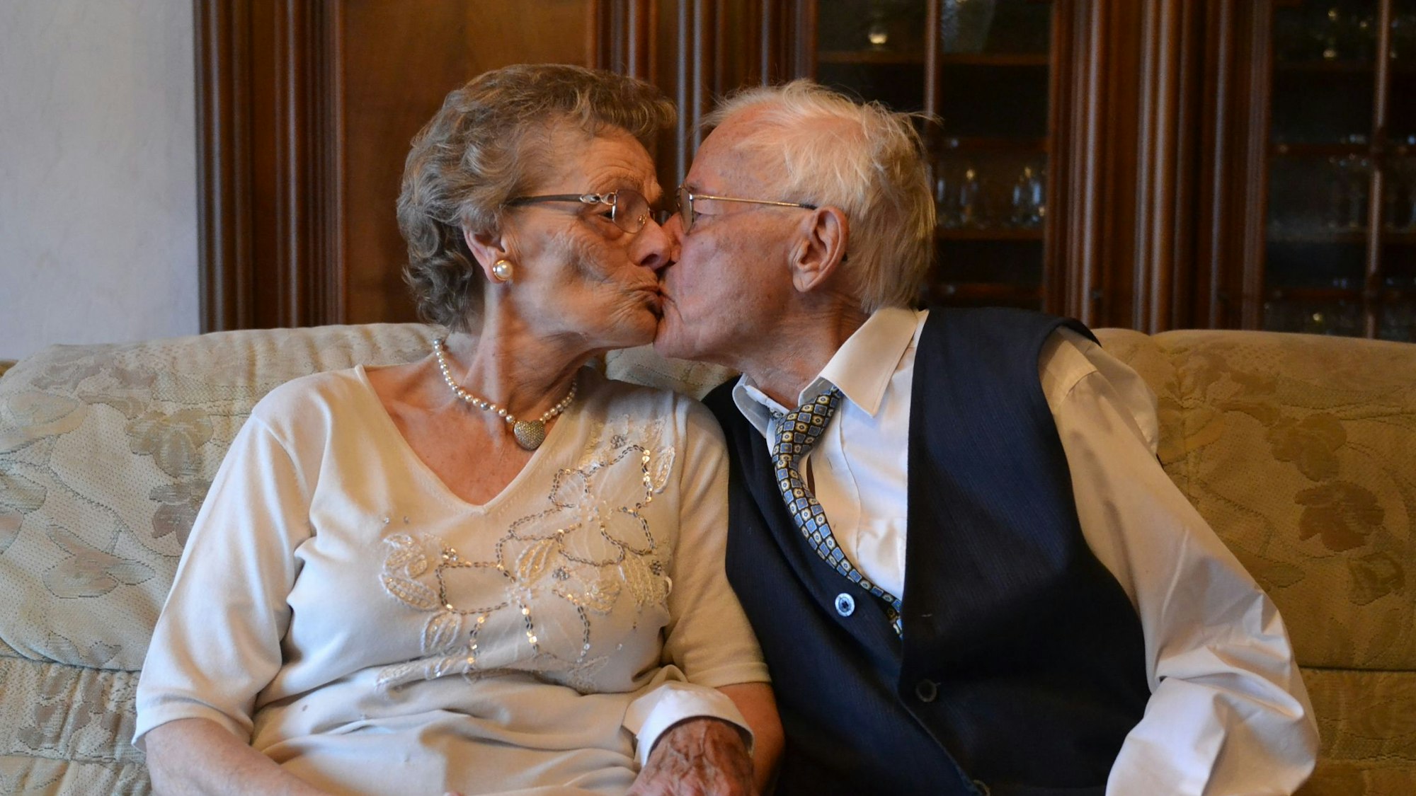 Eheleute Anna und Harry Spangenberg sitzen auf einer Couch und küssen sich.