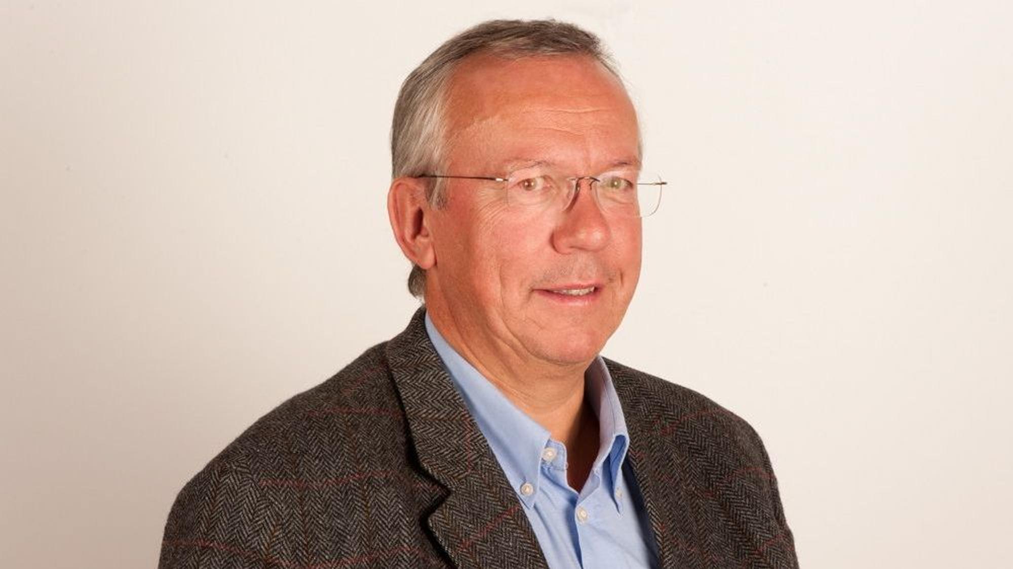Dr. Peter Melchers in einem blauen Hemd und dunklem Anzug.