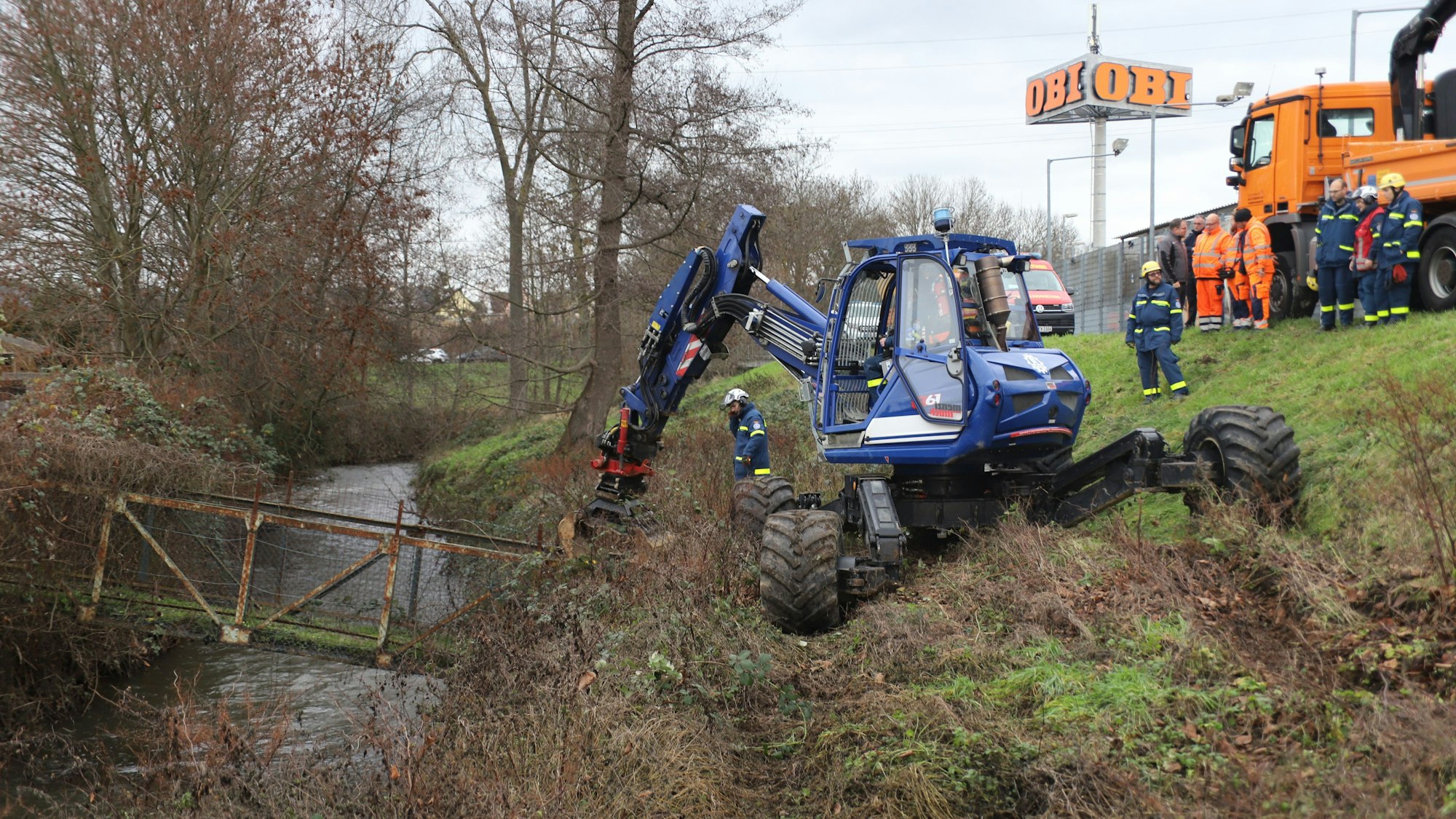 Ein blauer Bagger entfernt eine Brücke über einem Graben.