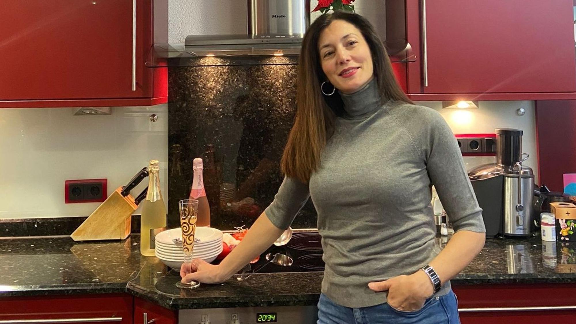 Eneka Krämer-Razquin steht in ihrer Küche mit roten Schränken, ein Glas Sekt in der Hand.