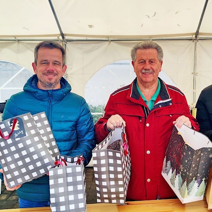 Martin Jost, Hubert Hamacher und Maria Surges-Brilon stehen unter einem Zelt und halten Weihnachtstüten in den Händen.