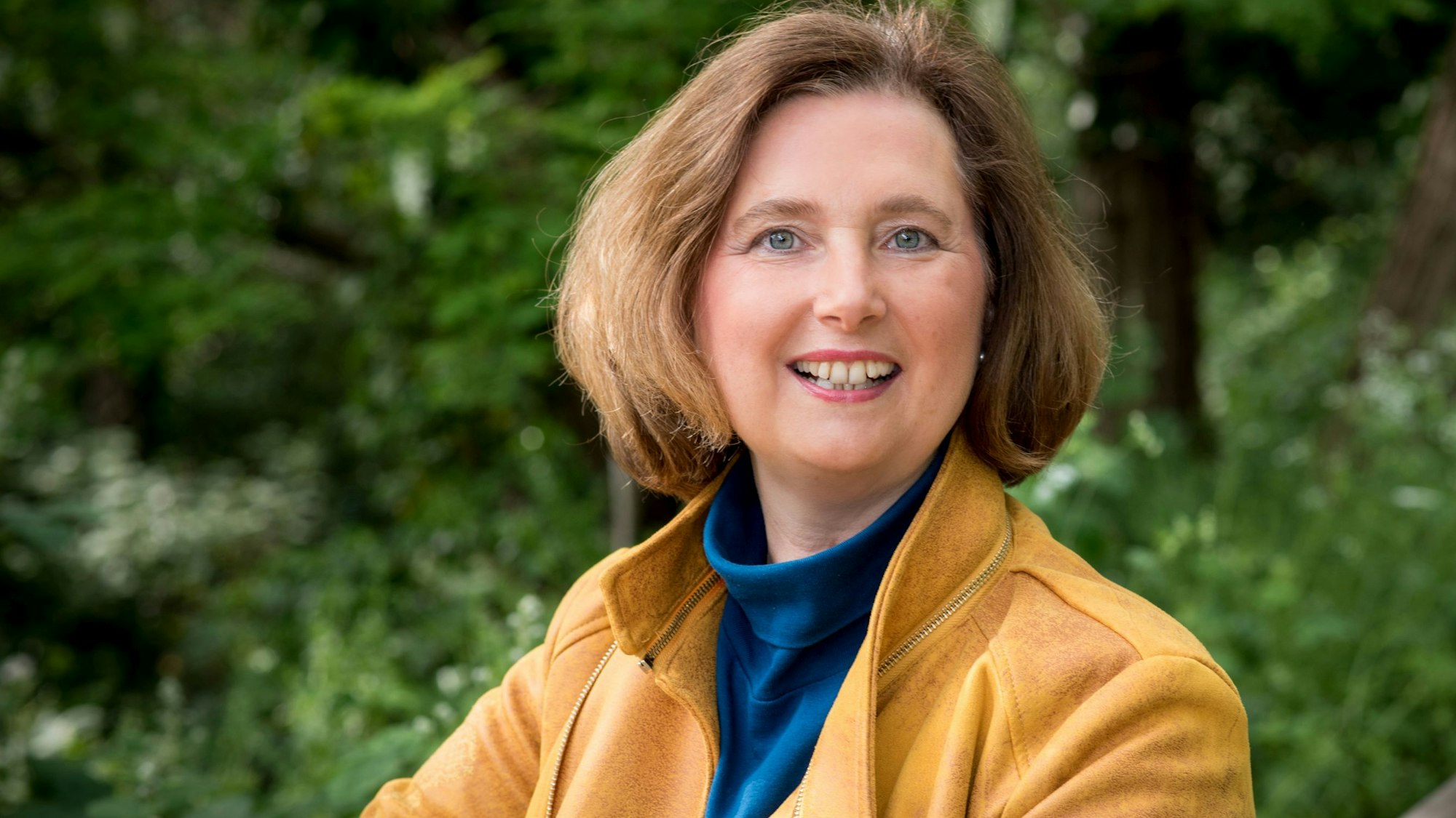 Eine Frau in einer hellbraunen Lederjacke vor einem grünen Hintergrund