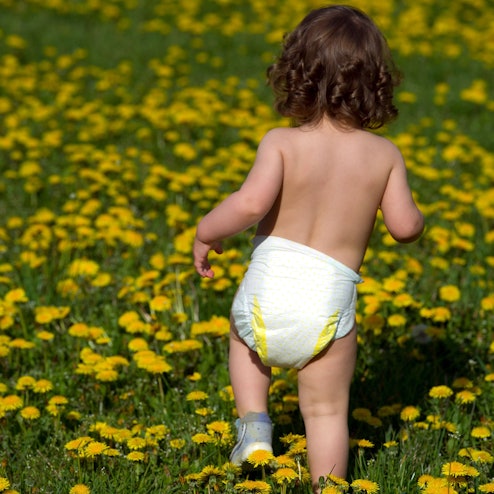 Ein kleines Mädchen, nur bekleidet mit einer Windel, läuft über eine Löwenzahnwiese.