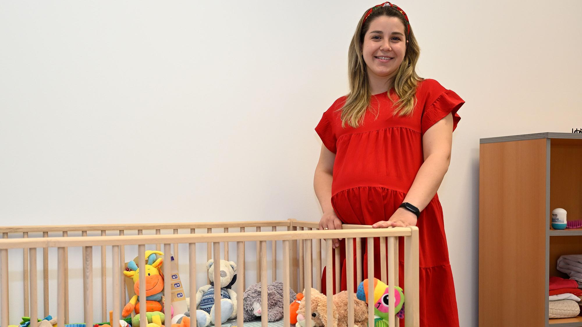 Yulia Zdzozhek (23) steht in einem roten Kleid an einem Kinderbett.