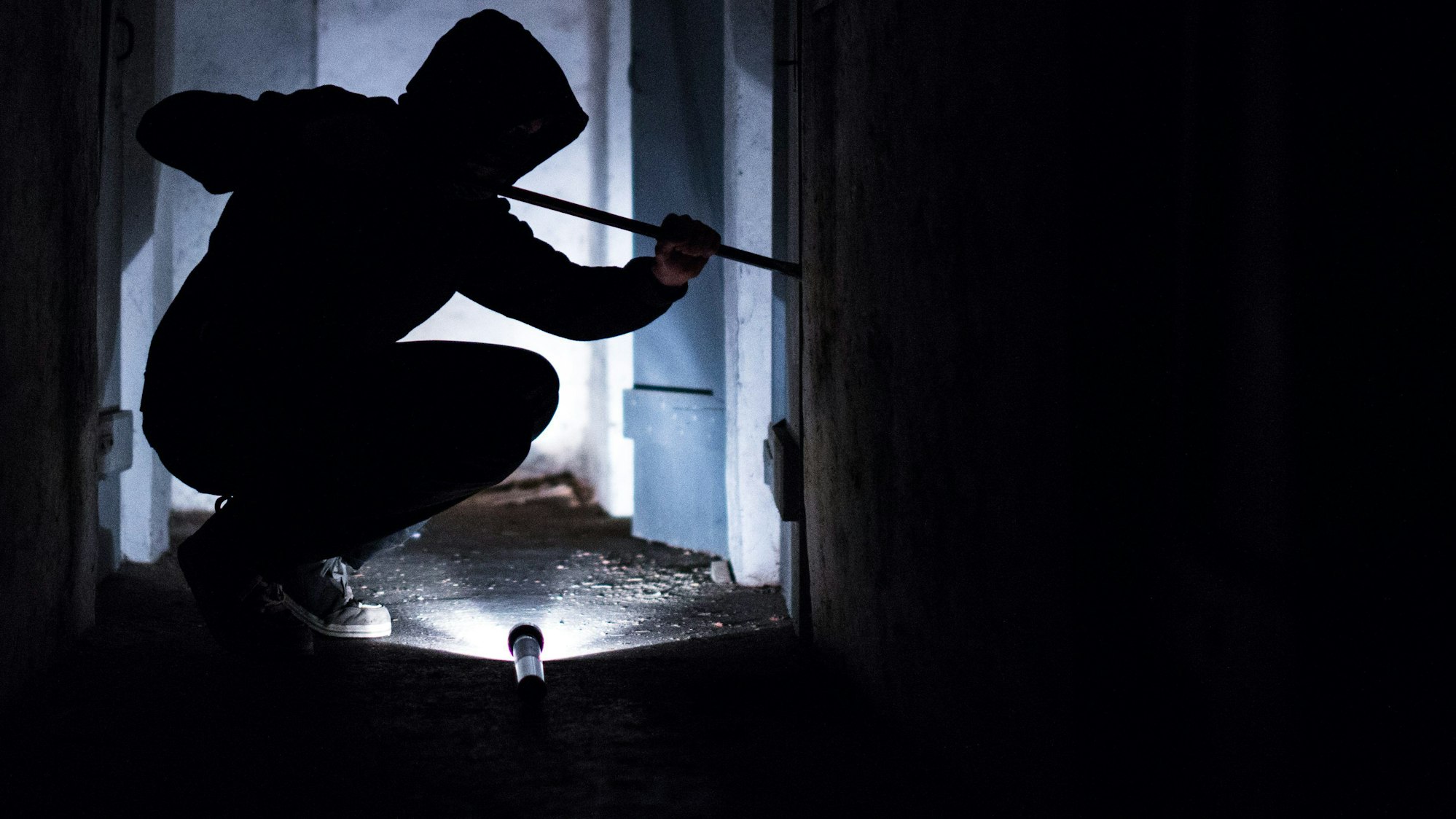 Ein Mann hebelt mit einem Brecheisen eine Tür im Keller eines Wohnhauses auf (gestellte Szene).