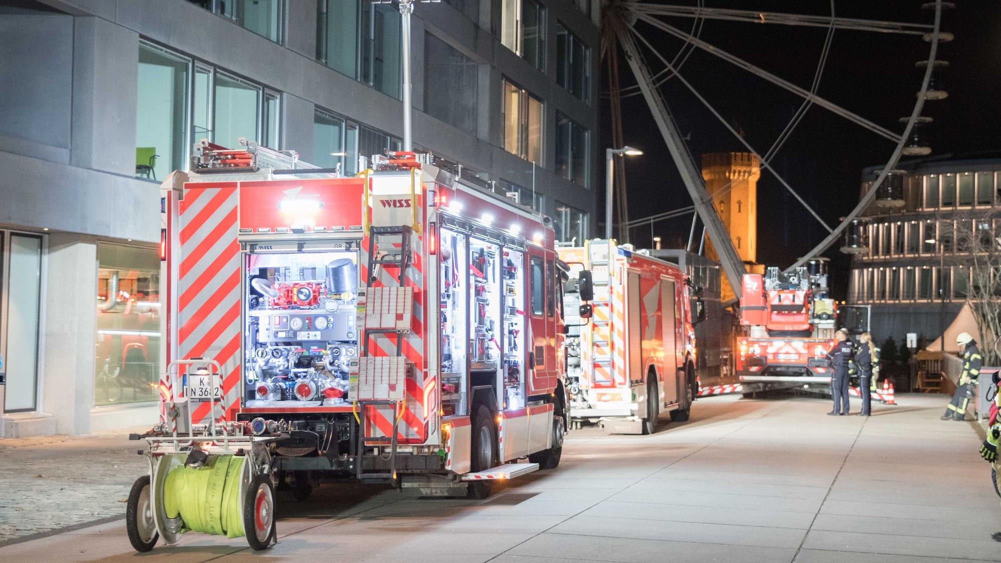 Die Kölner Feuerwehr sichert einen Brand in der Straße "Am Zollhafen" im Kölner Rheinauhafen. Im Hintergrund ist das Riesenrad am Schokoladenmuseum zu sehen.