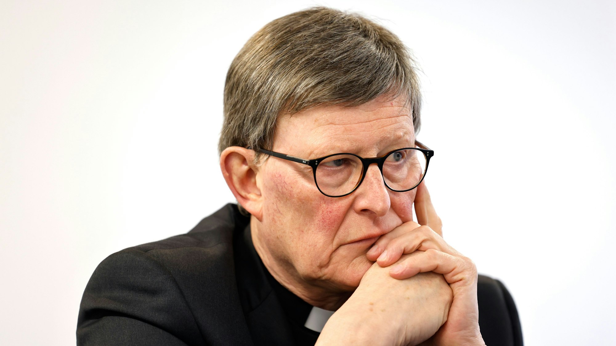 Kardinal Woelki schaut in die Ferne, seinen Kopf auf die Hand gestützt.