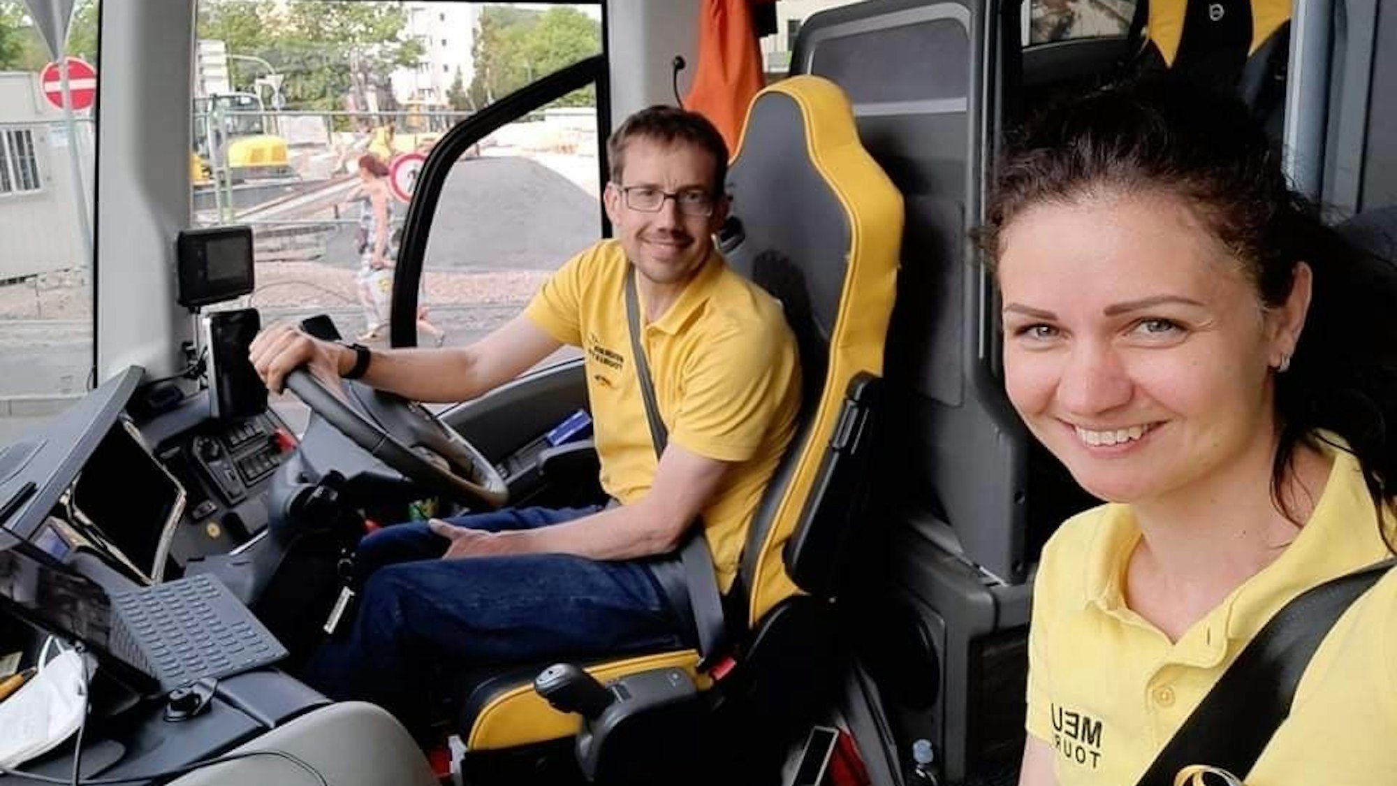 Ein Mann und eine Frau. beide in gelben Oberteilen, sitzen in einem Bus.