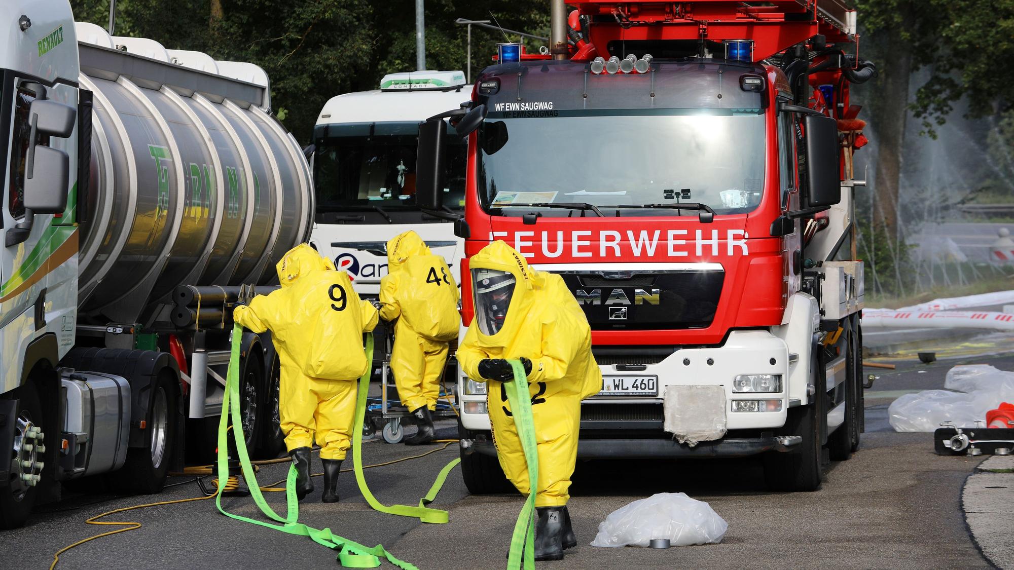 Einsatzkräfte in Schutzanzügen tragen einen Schlauch zu havarierten Tanklastzug.