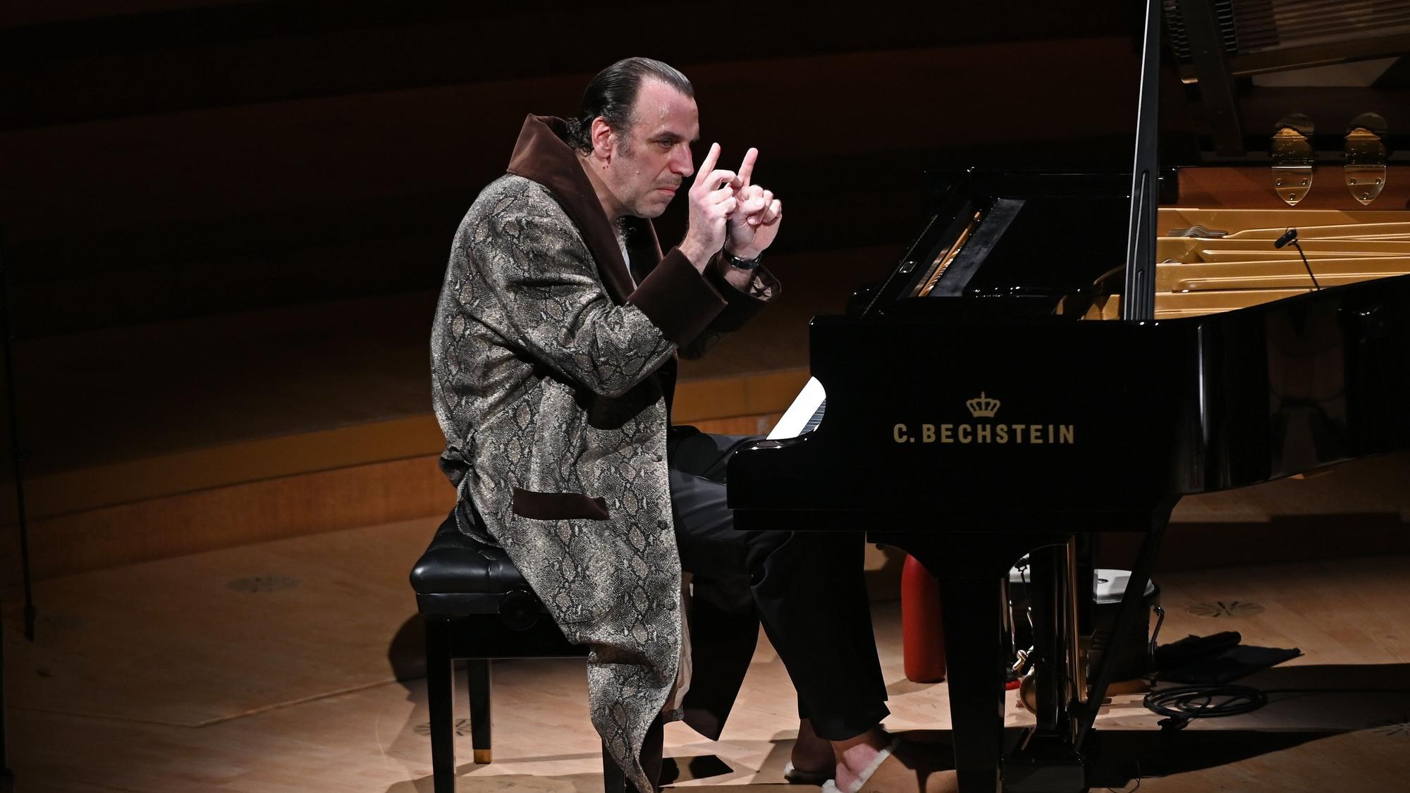 Der kanadische Musiker Chilly Gonzales sitzt am Konzertflügel in der Kölner Philharmonie. Er trägt einen Bademantel und Schlappen.