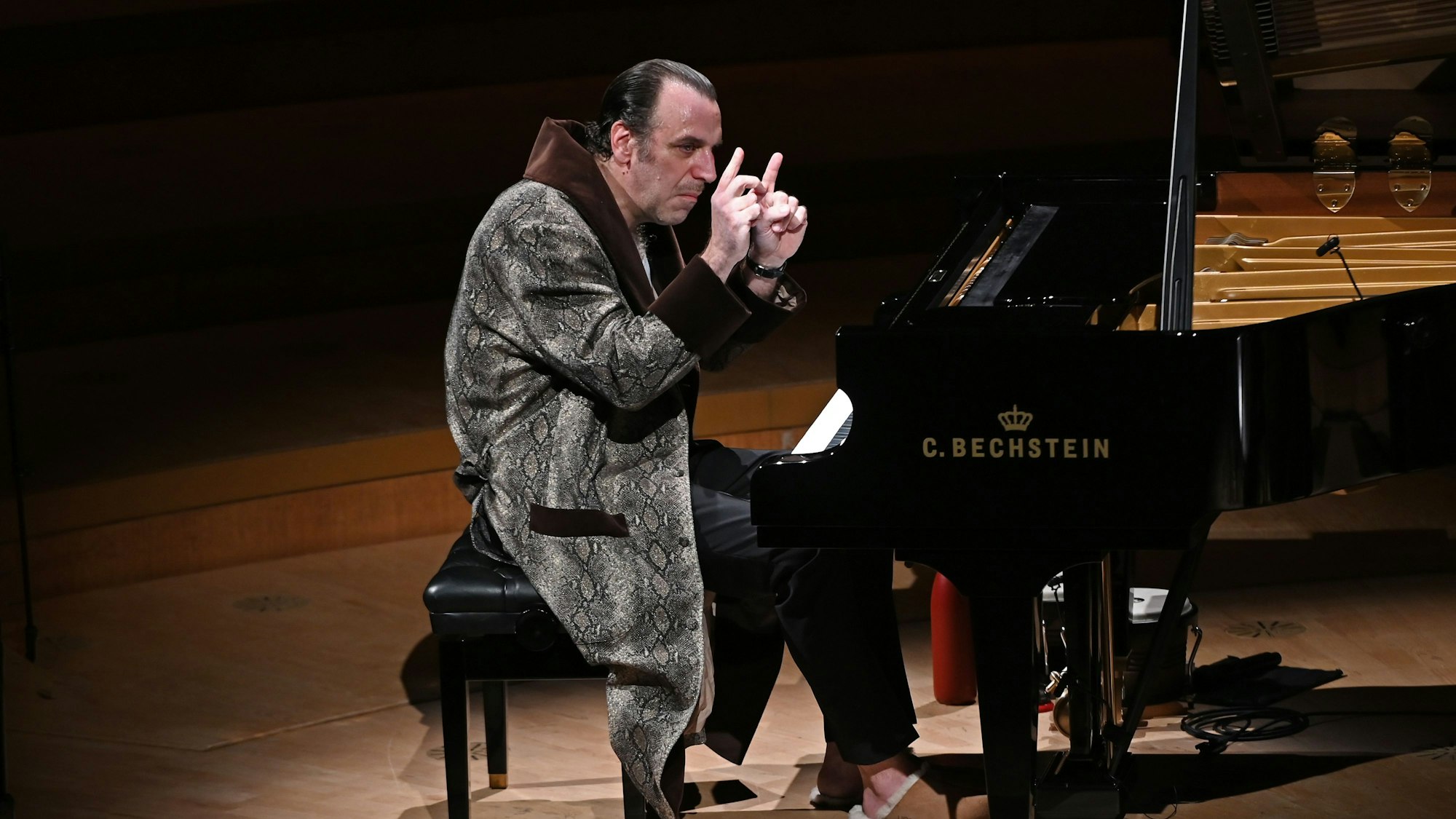Der kanadische Musiker Chilly Gonzales sitzt am Konzertflügel in der Kölner Philharmonie. Er trägt einen Bademantel und Schlappen.