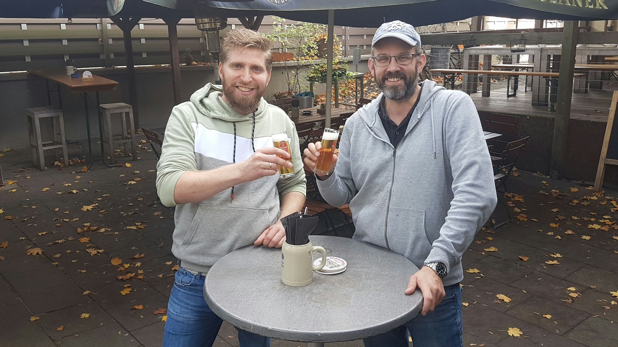 Die beiden Betreiber des KLausmann stehen im Hof und stoßen mit Kölsch an.