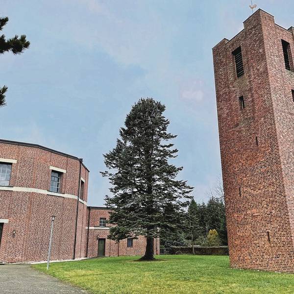 Rechts steht ein hoher, viereckiger Backsteinturm, links ein Rundbau ebenfalls aus Backsteinen. Das Gebäudeensemble liegt in einem kleinen Park, in dem ein hoher Nadelbaum steht.