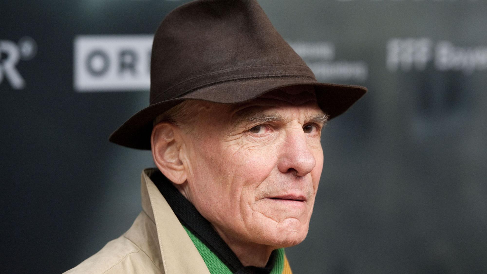 Der Schauspieler Hans Peter Hallwachs blickt in die Kamera. Er trägt einen schwarzen Hut.