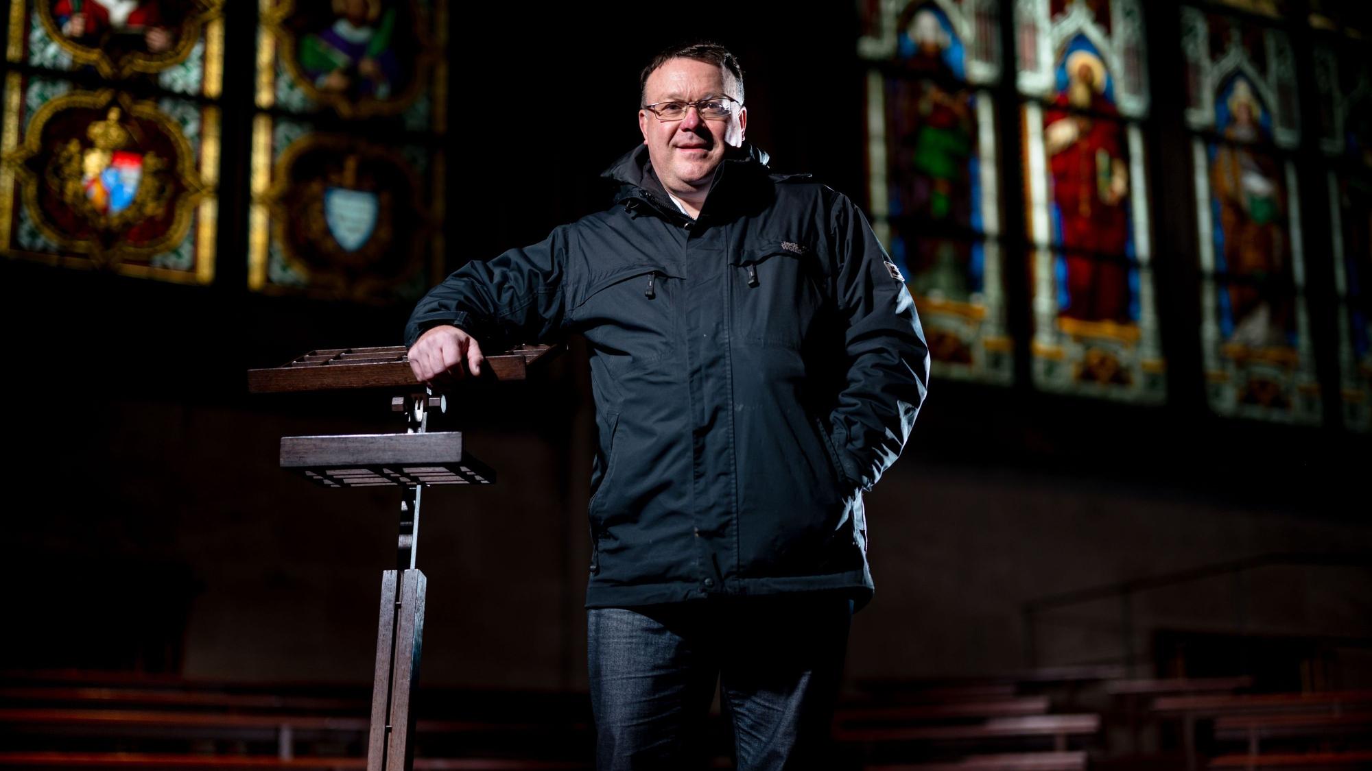 Domkantor Oliver Sperling steht an einem Dirigentenpult aus dunklem Holz im Kölner Dom.