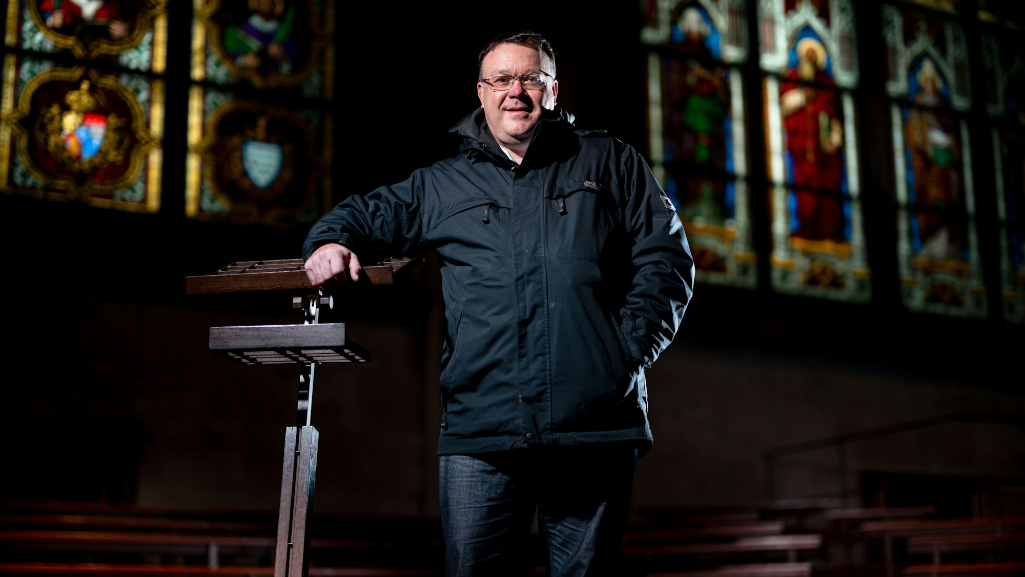 Domkantor Oliver Sperling steht an einem Dirigentenpult aus dunklem Holz im Kölner Dom.