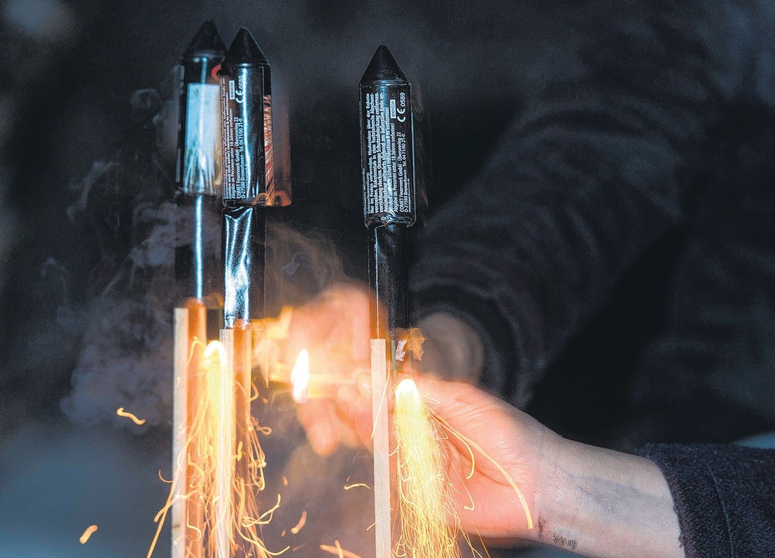 Eine Hand zündet mit einem Streichholz Feuerwerksraketen an.