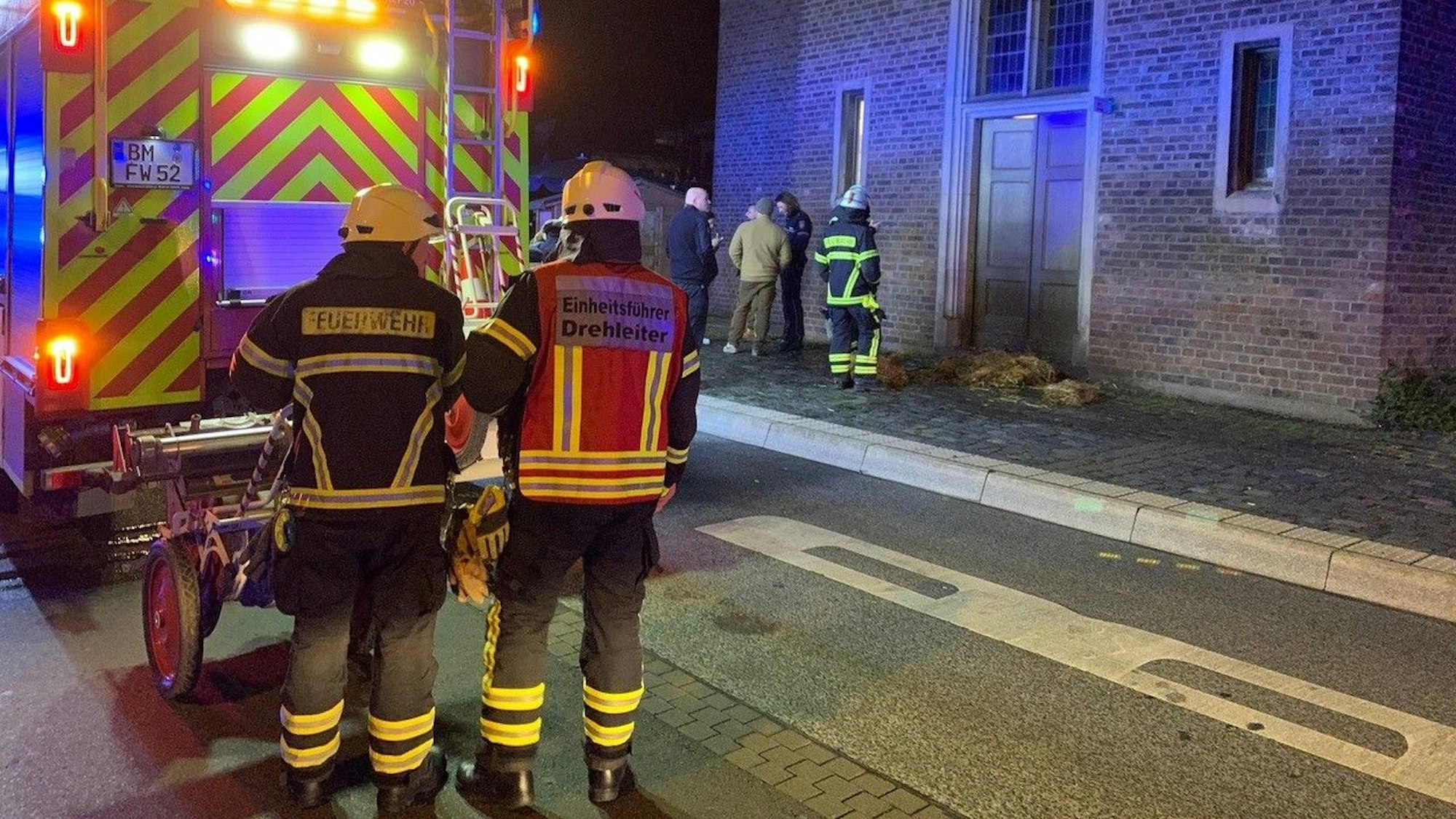 Feuerwehrleute stehen vor dem historischen Rathaus in Erftstadt. Stroh liegt vor der Tür.